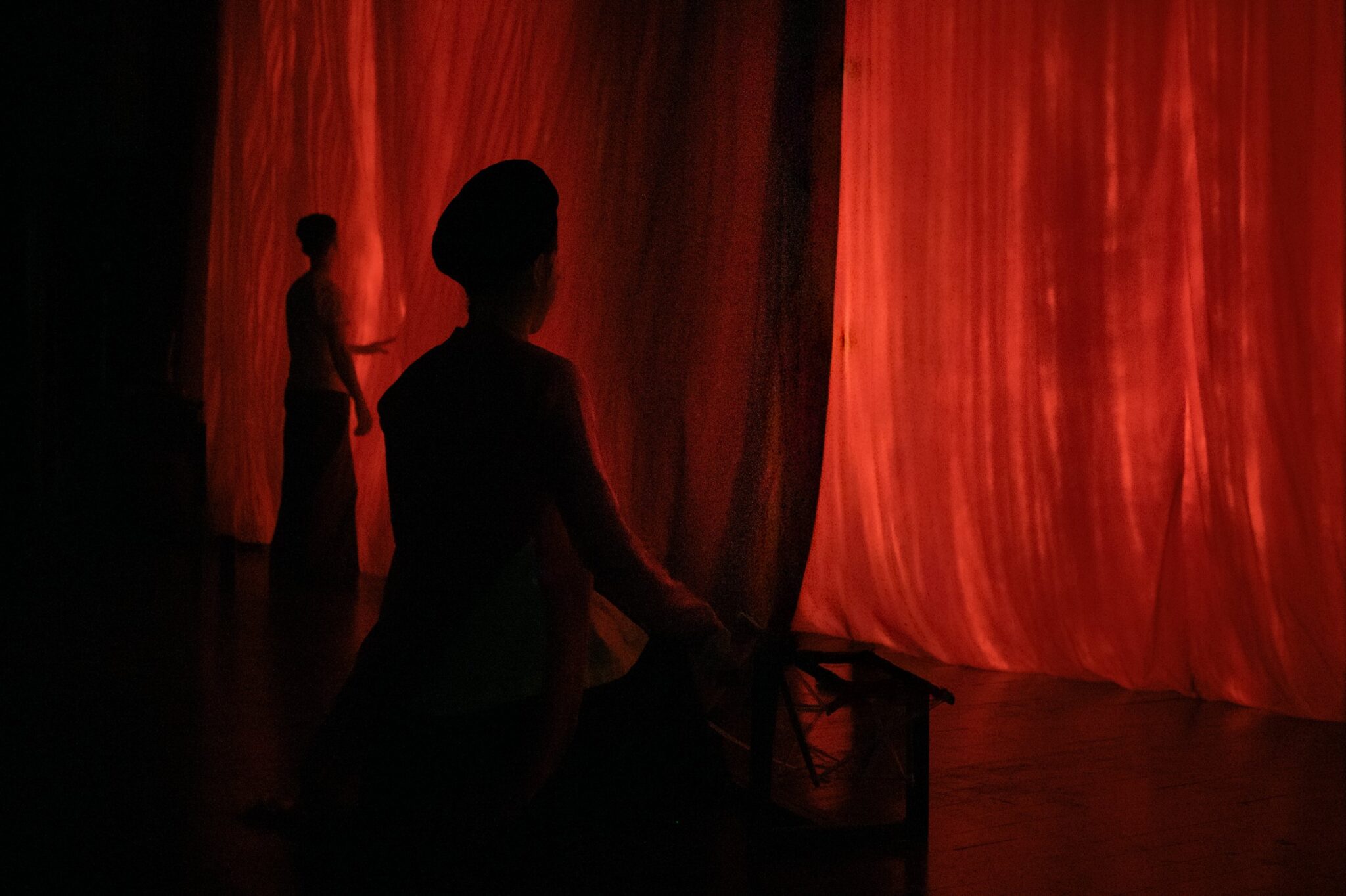 Silhouetted performers waiting in the wings before a red-lit stage curtain