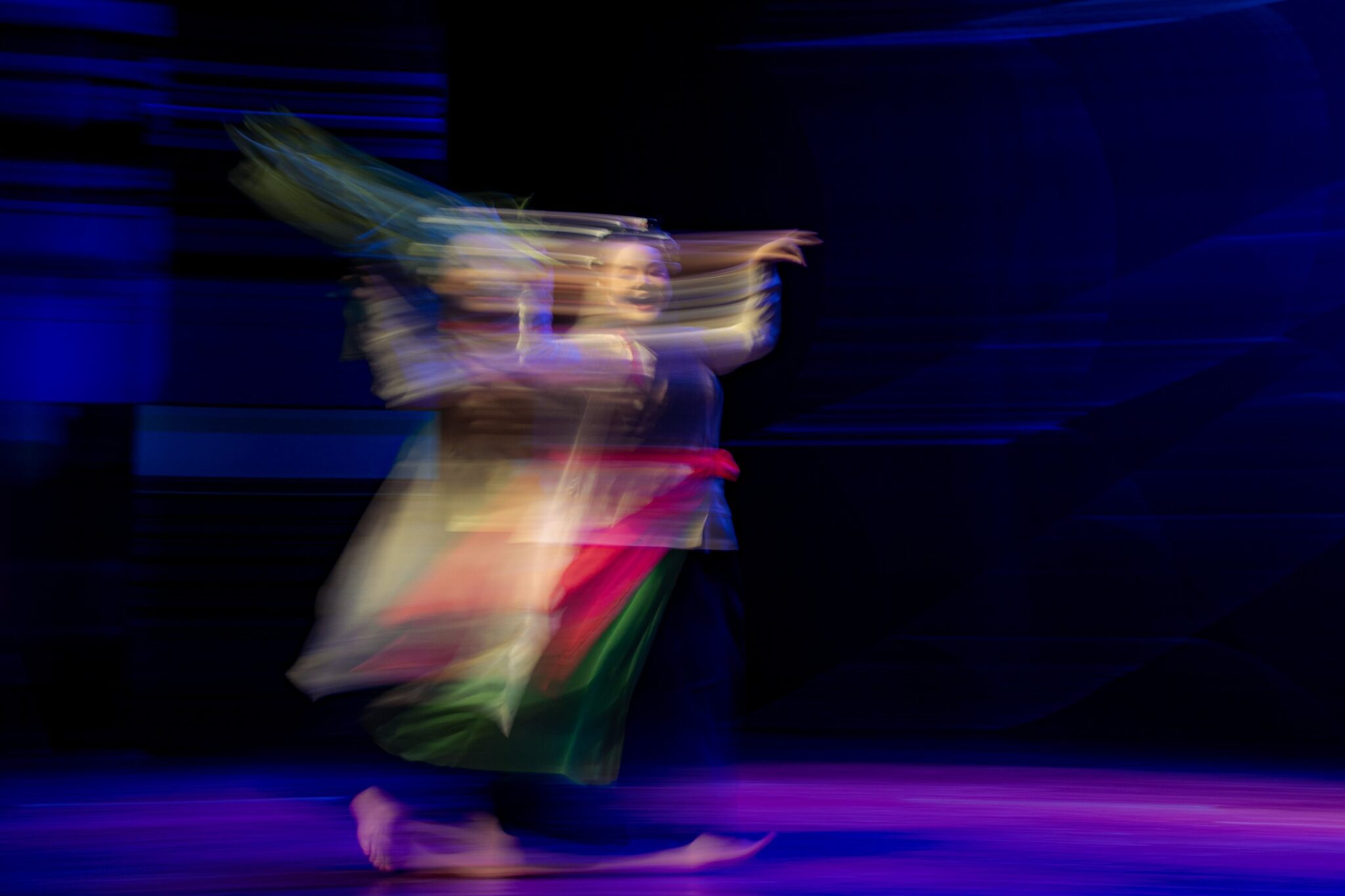 Performer in traditional costume caught mid-movement under blue stage light