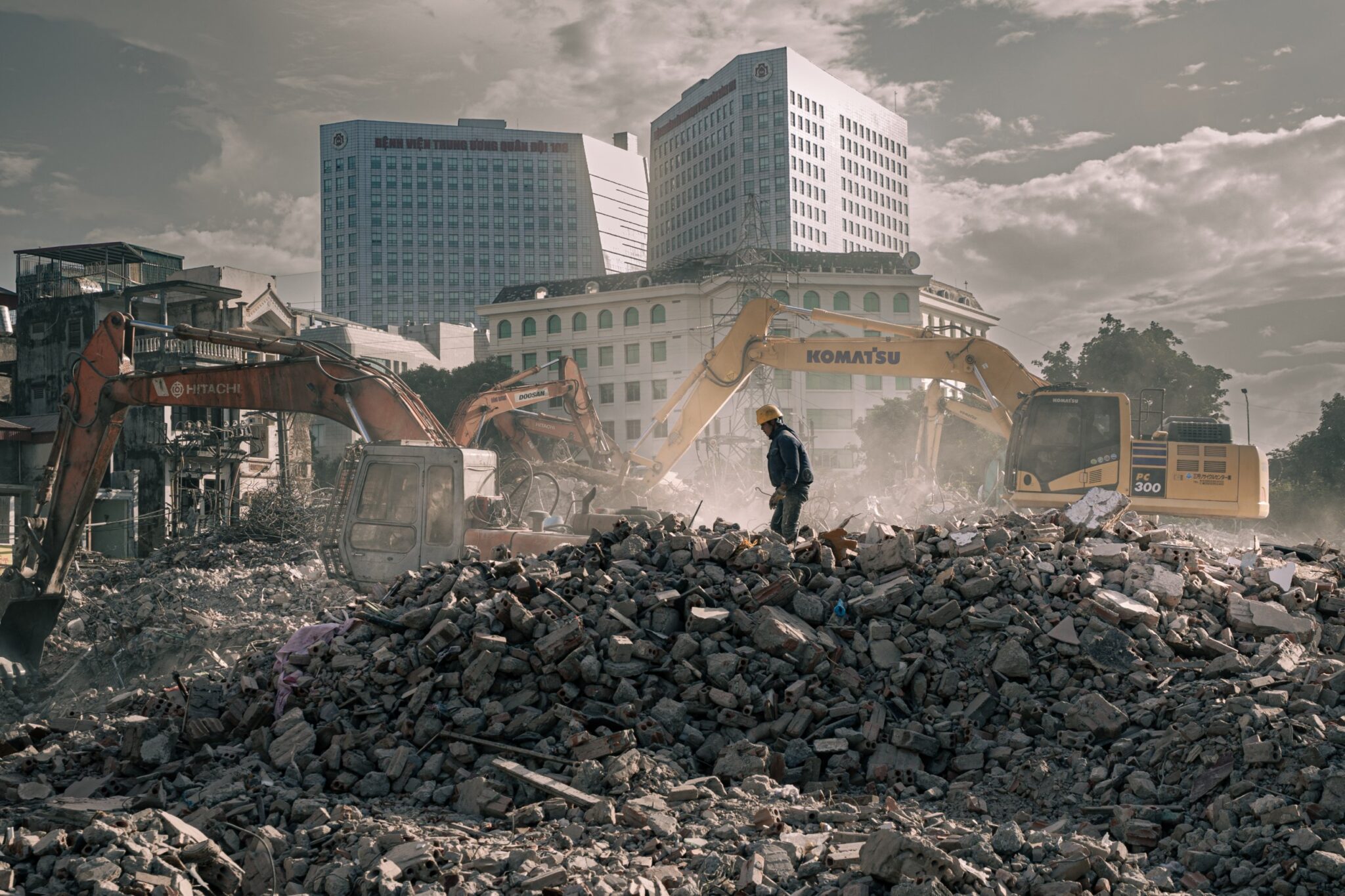 Worker standing on a rubble mound before excavators and a hospital tower