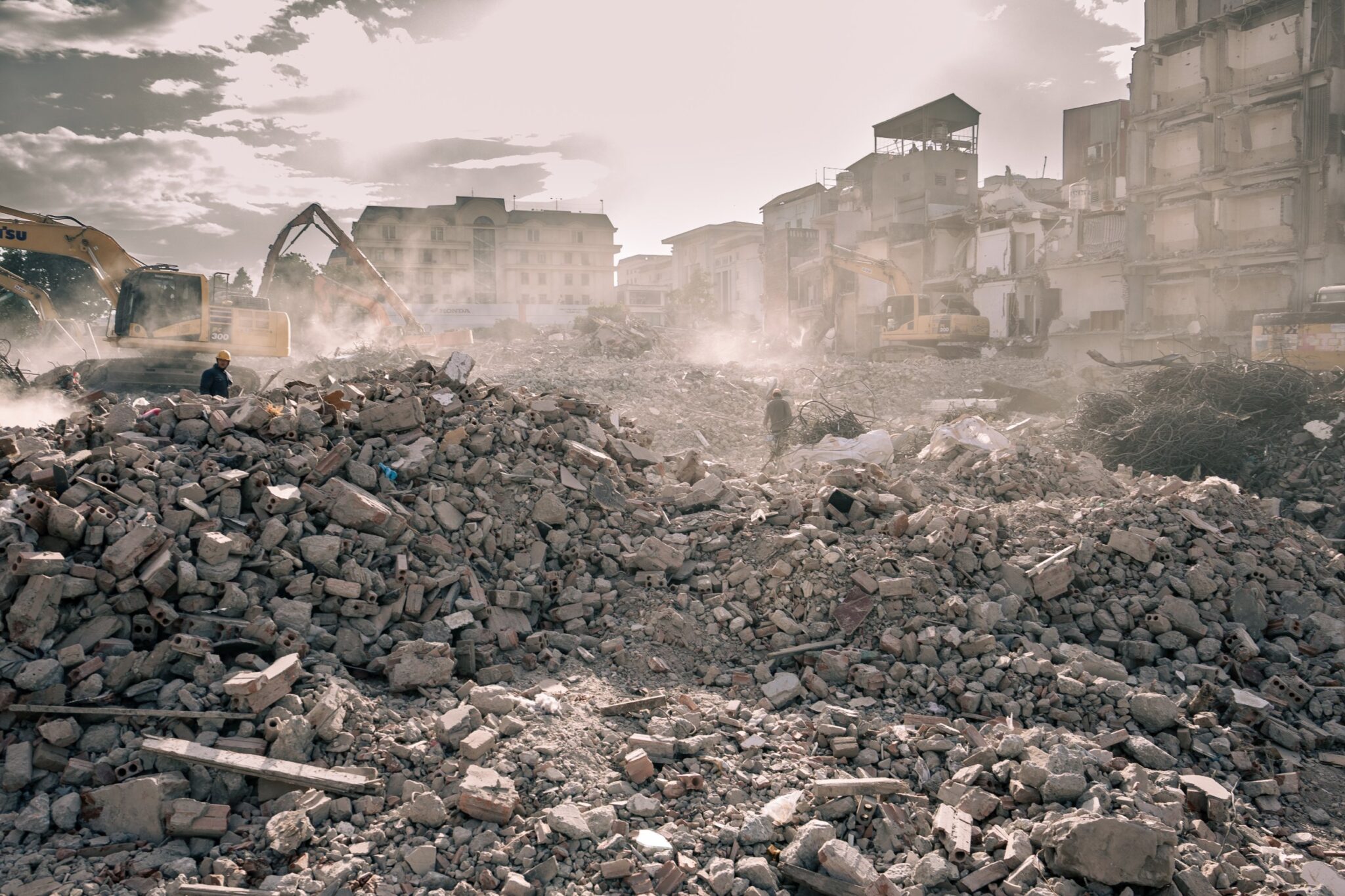 Excavators and half-demolished buildings in a field of rubble and dust