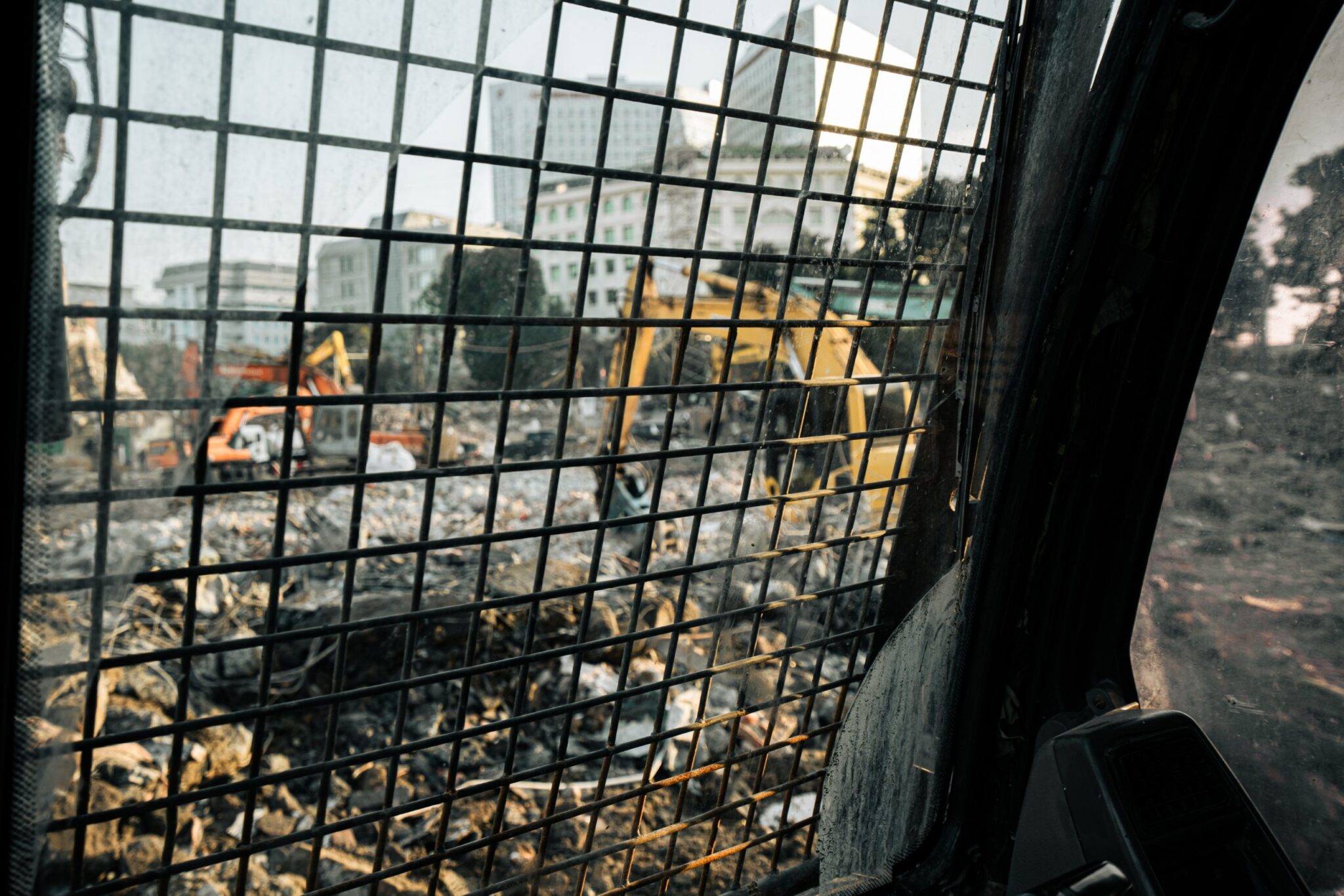 The demolition site seen through the mesh guard of an excavator cab