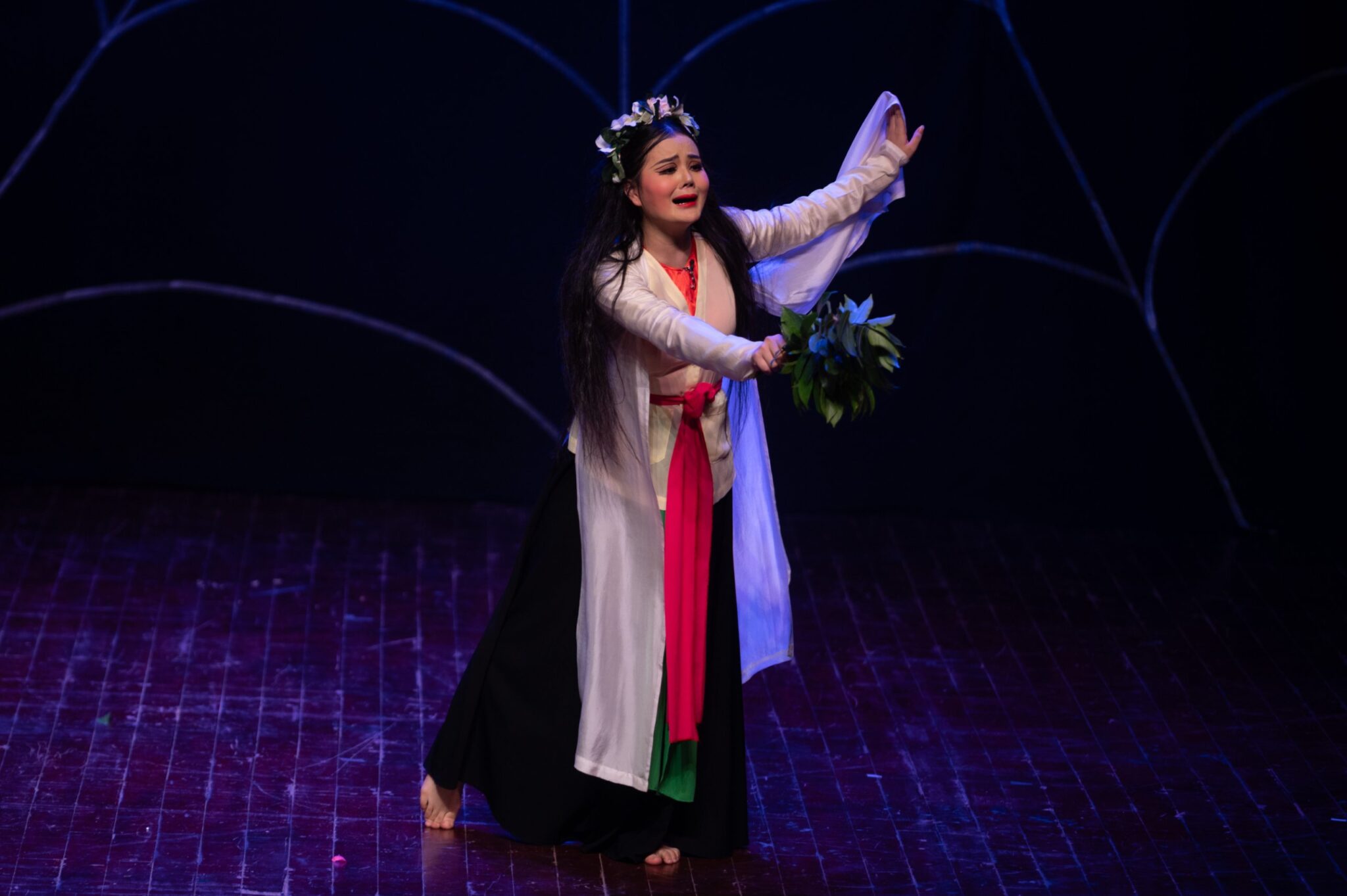 Actress playing Suý Vân on stage, crying, with a crown of flowers and a branch of leaves