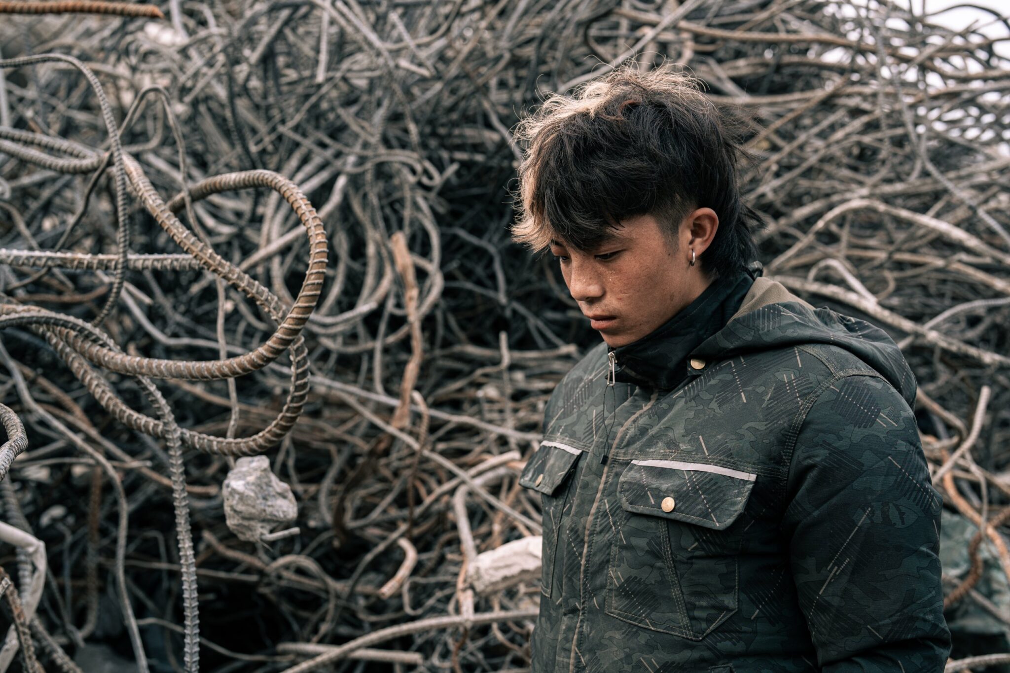 Young man with his head bowed in front of a tangle of salvaged steel rebar